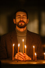 Wall Mural - Aesthetic Shot of Young Christian Man Lighting a Candle in Church, Praying and Expressing Devotion to the Lord. Parishioner Being Enlightened by the Teachings of Jesus Christ and Following his Path