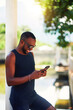 © oscargutzo - waist up portrait young black brazilian man in a park standing leaning on a pillar using or messaging on a cell phone  smiling relaxed in Ipanema