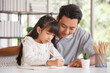 © aekkorn - Children education and home school concept : Young asisn father pleased to see little daughters' study success. Excited smiling small child girl enjoying learning and writing with pleasant dad at home
