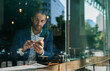 © mavoimages - Young businessman using his cellphone at a cafe counter