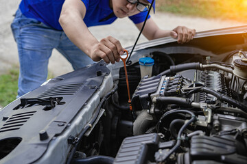 Young man checking and maintaining the quality of engine oil in his car Car repair and maintenance, oil change before long journey, car mechanic concept