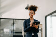 © Nuttapong punna - Confident beautiful African businesswoman typing laptop computer and digital tablet while holding coffee at office.
