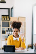 © Nuttapong punna - Attractive young African student studying at the college library, sitting at the desk, using a laptop computer, tablet and headphones having a video chat.