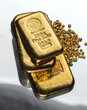 Several gold bars of different weight and a pile of pure gold granules on a mirror dark background. Selective focus.