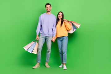 Poster - Full body portrait of two positive cheerful people hold arms boutique packages isolated on green color background