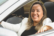 Uma mulher como motorista dentro de um carro de cor prata que está muito feliz e sorrindo para a câmera. Pessoa, Transporte, Veículo.