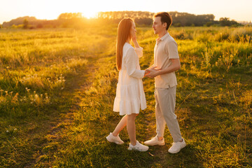 Wall Mural - happy young couple walking toward each other, hugging and kissing on beautiful green meadow in summe