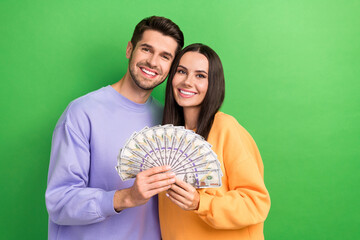 Poster - Portrait of two cheerful partners beaming smile hands hold dollar banknotes bills isolated on green color background