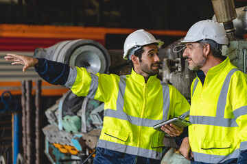 Two senior male engineers and workers wearing safety vests and jacket along with hardhat or helmet while clenching hands and making a fist standing in front of machine in warehouse