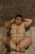 photo of  a plus size filipino woman with a shaved head sitting cross legged in the sun wearing nude bra and underwear