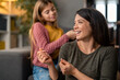 © Dorde - Sweet little girl out of focus sitting on sofa in living room playing with mom's hair, having fun, enjoying their time together. Mother and daughter bonding time at home.