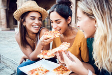Three Cheerful Multiracial Young Women Eating Italian Pizza At City Street. Young Female Friends Enjoying Summer Holidays. Vacation Lifestyle Concept