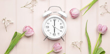 Alarm Clock And Flowers On Light Wooden Background. Spring Time