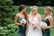 Close view of stunning bridesmaids in elegant silk gowns with bouquets of flowers, posing with bride on nature during wedding day