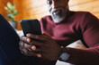 © Wavebreak Media - Close-up of african american senior man using smartphone while sitting on couch at log cabin