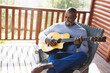 © Wavebreak Media - Bald african american senior man singing and playing guitar while sitting on chair in balcony
