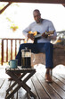 © Wavebreak Media - Close-up of french press, mug on table with african american senior man playing guitar in background