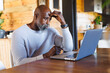 © Wavebreak Media - Stressed bald african american senior man with head in hand looking at laptop in log cabin