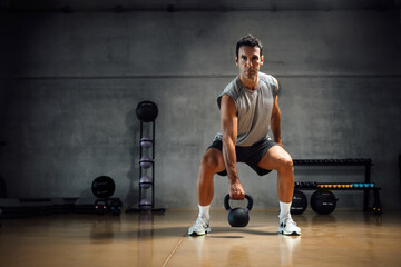 Athletic man lifting weight with kettle bell in gym.