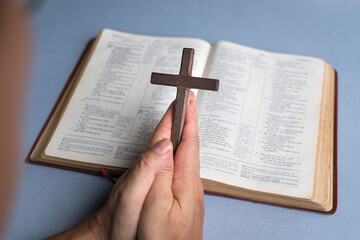 Man praying holding cross crucifx with open bible at the background. Christian faith concept.