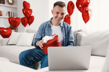 Wall Mural - Valentine's day celebration in long distance relationship. Man opening gift from his girlfriend at home