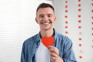 Poster - Handsome young man with decorative heart indoors, view from camera. Valentine's day celebration in long distance relationship