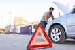 © Alan - young man inspecting the engine of his car, hazard triangle on the road, car insurance concept