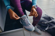 © Drazen - Close up of black athletic woman tying shoelace on sneakers while preparing for workout at health club.