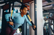 © Drazen - Black sportswoman doing TRX exercises with suspension straps in gym.
