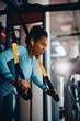 © Drazen - African American athletic woman using suspension straps while working out in gym.