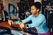 © Drazen - Smiling black sportswoman working out on exercise bicycle in gym.