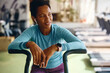 © Drazen - Black athletic woman taking break after exercising on stationary bike in gym.