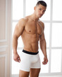 Handsome guy wearing white boxers. Sexy muscular man with six pack abs posing in underwear in light room. Shirtless male model in studio.