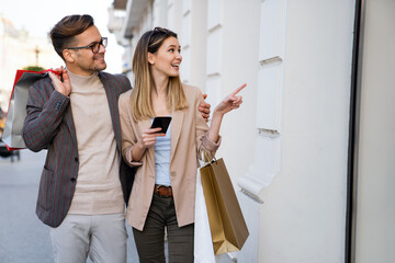 Wall Mural - Beautiful young loving couple carrying shopping bags and enjoying time together.