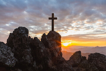 Silhouettes of crucifix symbol on top mountain with bright sunbeam on the colorful sky background