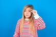 © Jihan - Upset caucasian teen girl wearing striped shirt over blue studio background shapes little gesture with hand demonstrates something very tiny small size. Not very much