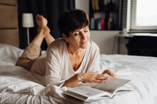 Smiling mature woman reading book while lying on bed