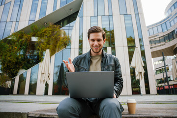 Cheerful man making videocall via laptop while sitting outside