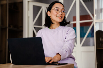 Poster - Smiling asian woman working on laptop while sitting at home