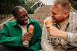 © Maskot - Happy multiracial male friends enjoying ice creams while sitting on steps