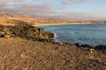 beautiful sunset on yellow sand beach from the cliff, with ocean and mountains in the background. El Cotillo, Fuerteventura, Canary Islands, Spain