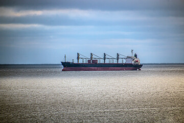 Wall Mural - a blue-red ship sails on the Black Sea with cranes on board under a blue cloudy sky