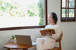 © PHAISITSAWAN - Elderly women sit and relax, stressed, watching series on laptops, reading and taking notes in notebooks and sipping tea happily inside the house with the brightest light and fresh air.