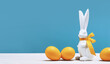 White Easter bunny with yellow ribbon bow with dyed orange eggs on white table. Happy Easter banner with copy space