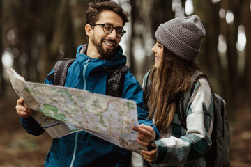 Happy inspired young european couple tourists in jackets with backpack walk in autumn forest, enjoy cold season