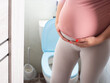 Pregnant girl with a big belly on the background of the toilet. The concept of frequent urination in pregnant women. Copy space for text
