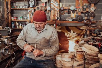 A senior man sitting in the workshop and processing wooden utensils in the old manual way