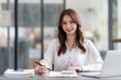 © amnaj - Pretty Asian businesswoman sitting smiling and happy working on laptop computer and document in office. Looking at camera.