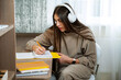 © Oksana Klymenko - Teenage girl sits at desk at home and write in a notebook. White headphones on head for listen relax music. Thinks about plans, keeps a diary book.