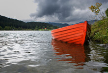 Red Rowboat Anchored On The Shore Of A Lake